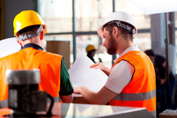 Trabalhadores usando capacetes e coletes de segurança analisam documentos em ambiente industrial, representando atuação da CIPA na prevenção.