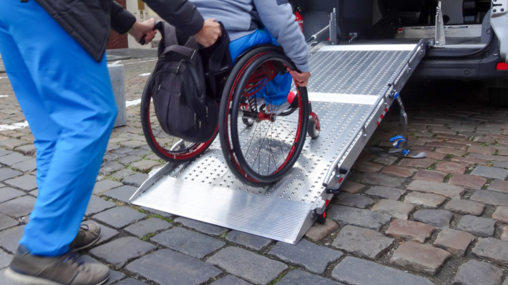 Pessoa em cadeira de rodas sobe rampa de acesso para veículo adaptado com auxílio, representando acessibilidade, mobilidade e inclusão.