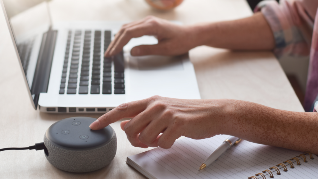 Pessoa utiliza assistente virtual por comando de voz ao lado de notebook, destacando tecnologia assistiva e acessibilidade digital.