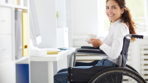 Feliz jovem empresária com uma xícara de chá olhando para a câmera enquanto está sentado no local de trabalho no escritório