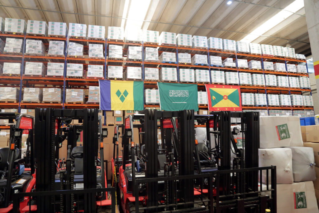 A imagem representa as 292 toneladas de suprimentos médicos entregues em grandes galpões. Mostra as bandeiras das ilhas ajudadas, Granada; São Vicente e Granadinas e o país que moveu-se a esta ação, a Arábia Saudita.