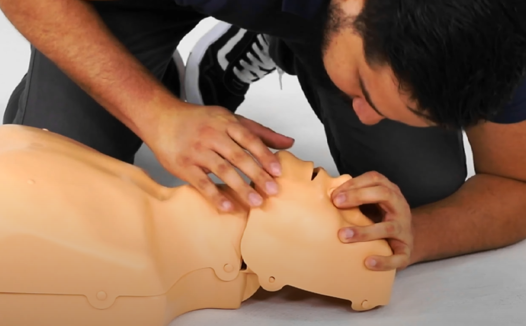 Imagem demonstra a abertura das vias aéreas na ressuscitação cardiopulmonar (RCP) em adulto, com técnica de inclinação da cabeça e elevação do queixo em manequim de treinamento. Etapa essencial do suporte básico de vida.