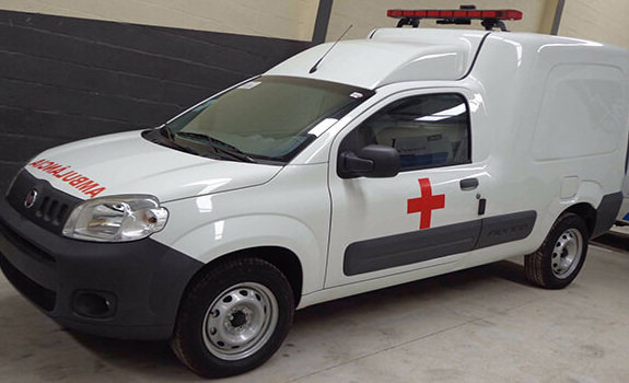 Ambulância branca com símbolo da cruz vermelha e sinalização luminosa no teto, utilizada para transporte médico e atendimento pré-hospitalar. Veículo equipado para suporte básico em situações de emergência.