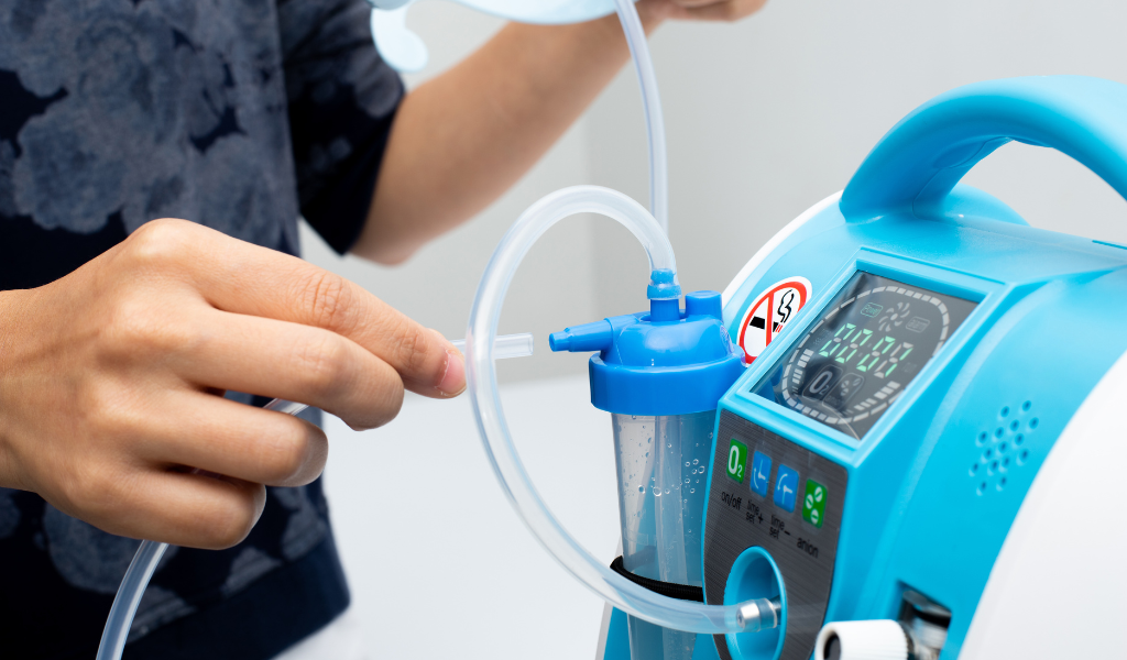 Close-up de concentrador de oxigênio com frasco umidificador e conexão da tubulação nasal sendo ajustada. Equipamento utilizado para oxigenoterapia domiciliar e hospitalar, auxiliando pacientes com dificuldades respiratórias.