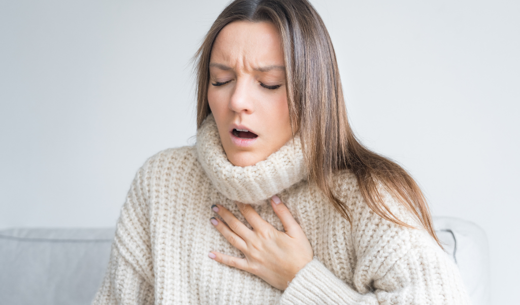Mulher com expressão de desconforto respiratório e mão sobre o peito, ilustrando sintoma de dispneia ou falta de ar. A imagem representa possível emergência médica relacionada a doenças cardíacas ou pulmonares.