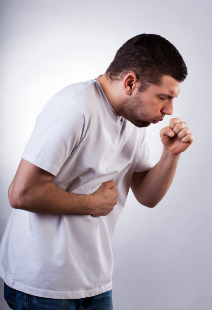Homem adulto com expressão de desconforto leva a mão ao peito enquanto tosse. A imagem representa sintomas respiratórios como gripe, bronquite ou outras condições pulmonares, em fundo neutro.