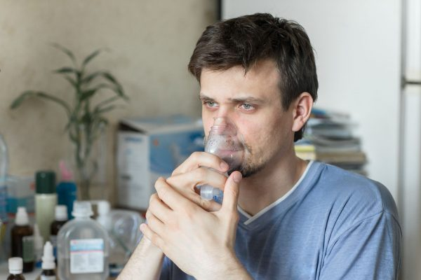 Imagem mostra homem realizando inalação com nebulizador para tratamento respiratório. Terapia indicada para asma, bronquite e outras doenças pulmonares, auxiliando na melhora da respiração e alívio dos sintomas.