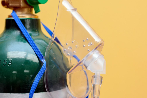Imagem mostra máscara de oxigênio conectada a cilindro para oxigenoterapia. Equipamento utilizado no suporte respiratório e atendimento de emergência, essencial em primeiros socorros e ambientes hospitalares.