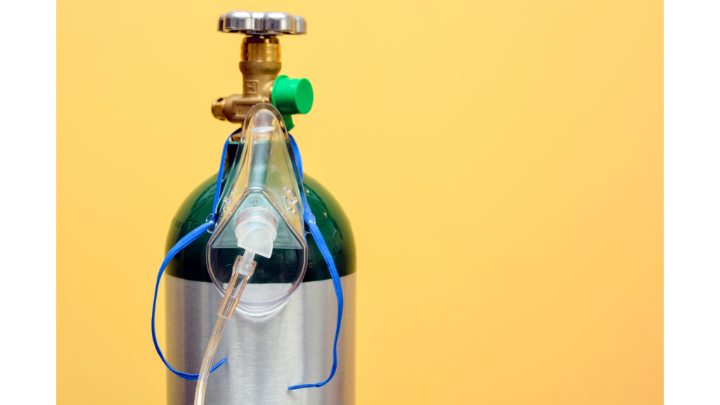 Imagem de cilindro de oxigênio medicinal com máscara facial acoplada para oxigenoterapia. Equipamento utilizado no tratamento de hipoxemia, insuficiência respiratória e suporte em atendimentos hospitalares e domiciliares.
