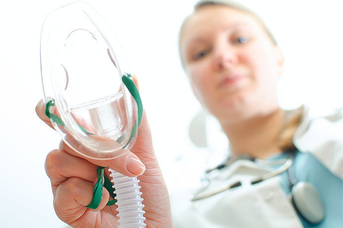 Imagem mostra profissional de saúde segurando máscara de oxigênio para oxigenoterapia. Equipamento utilizado no suporte respiratório em hospitais e emergências, auxiliando na oferta de oxigênio ao paciente.