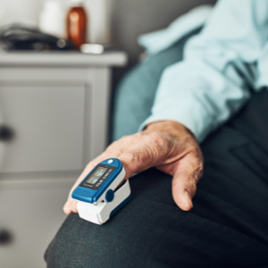 Pessoa utilizando oxímetro de dedo para monitoramento da saturação de oxigênio (SpO2) e frequência cardíaca. Equipamento amplamente usado no acompanhamento domiciliar e hospitalar de pacientes com doenças respiratórias e cardiovasculares.