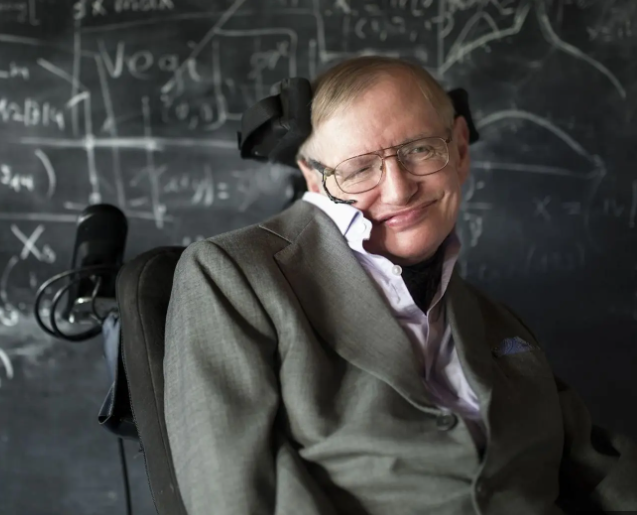 Homem em cadeira de rodas, vestindo terno e óculos, posicionado diante de quadro com fórmulas matemáticas e científicas. Representa pesquisa, ciência, superação e contribuição intelectual na área acadêmica.