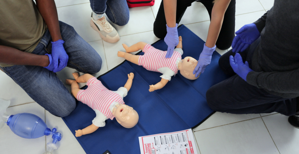 Imagem de treinamento de RCP pediátrica com manequins infantis em curso de primeiros socorros. Participantes realizam compressões torácicas e práticas de suporte básico de vida para atendimento de parada cardiorrespiratória em bebês.