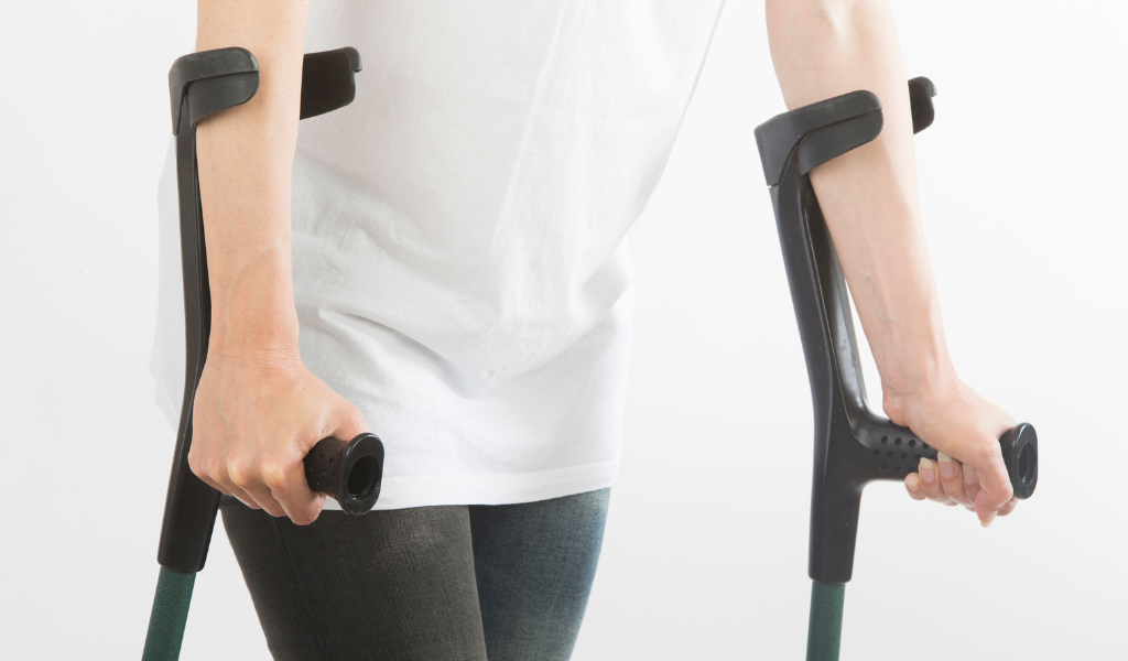 Imagem mostrando o uso correto de muletas axilares, com apoio adequado nas mãos e posicionamento abaixo das axilas. Ilustra técnica apropriada para auxiliar na locomoção e reduzir risco de lesões.