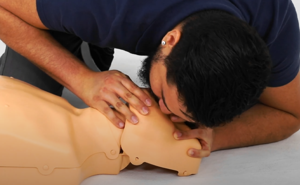 Imagem demonstra ventilação boca a boca na ressuscitação cardiopulmonar (RCP) em adulto, realizada em manequim de treinamento. Técnica essencial de primeiros socorros no atendimento à parada cardiorrespiratória.