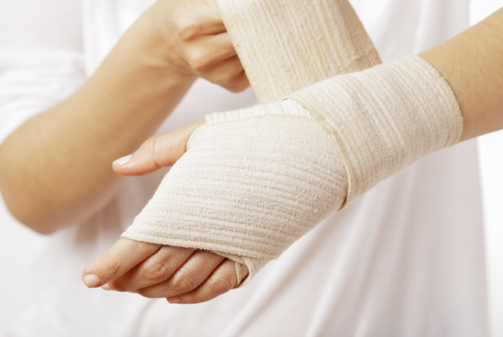 Atadura elástica sendo aplicada na mão para curativo e imobilização. Material utilizado em primeiros socorros, tratamentos médicos e suporte a lesões, auxiliando na compressão, proteção e estabilização da região afetada