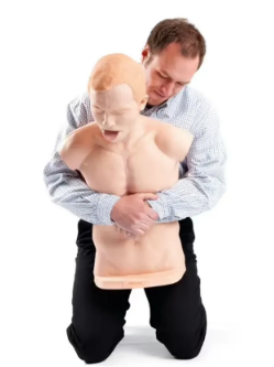 Instrutor realizando treinamento da manobra de Heimlich em manequim de primeiros socorros. A técnica é utilizada para desobstrução das vias aéreas em casos de engasgo, simulando a compressão abdominal aplicada em situações de emergência.