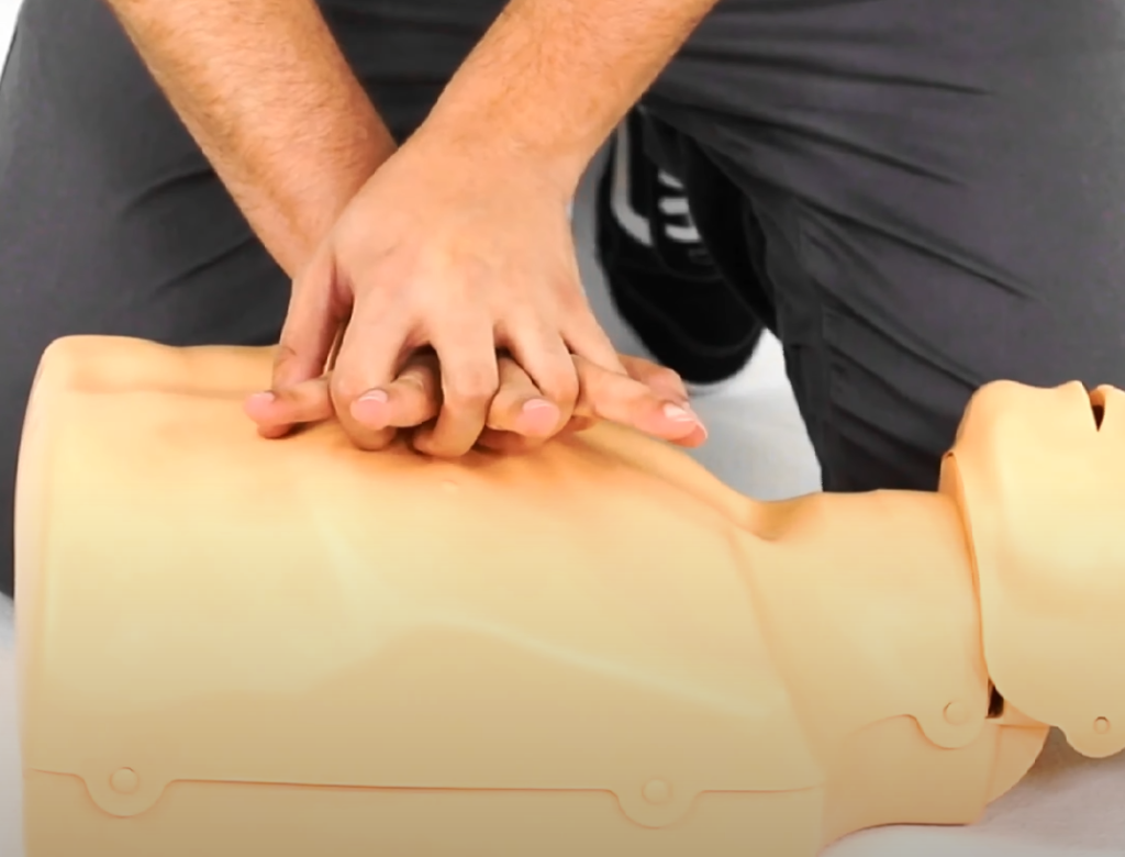 Imagem demonstra compressões torácicas na ressuscitação cardiopulmonar (RCP) em manequim de treinamento. Técnica essencial de primeiros socorros para parada cardiorrespiratória e suporte básico de vida em adultos.
