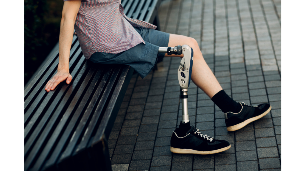 Pessoa sentada em banco ao ar livre com prótese na perna, representando reabilitação, mobilidade assistiva e inclusão social.
