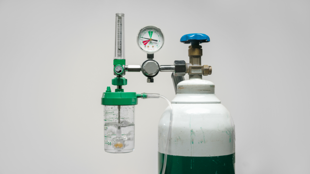 Cilindro de oxigênio medicinal equipado com regulador de pressão, manômetro, fluxômetro e frasco umidificador. Conjunto utilizado na oxigenoterapia para controle do fluxo em L/min e oferta segura de oxigênio ao paciente.